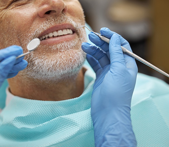 Dentist performing dental checkup on older male patient